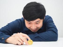 asiatico uomo seduta a il scrivania e guardare a d'oro bitcoin nel mano con sorridente foto