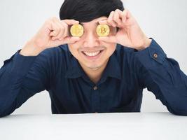 asiatico uomo allegro sorridente viso vicino il suo occhi di oro bitcoin seduta a il scrivania foto