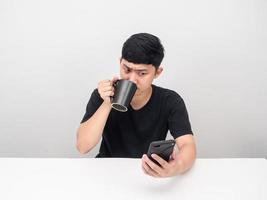 uomo potabile caffè tazza gesto pensiero e guardare a mobile Telefono foto