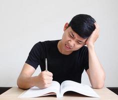giovane uomo con penna grave e sentire sforzo con problema toccare il suo testa di mano con il libro su il scrivania su bianca isolato foto