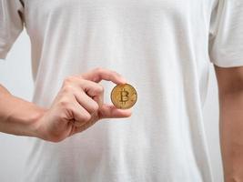 vicino su uomo bianca camicia mostrare d'oro bitcoin nel il suo mano foto