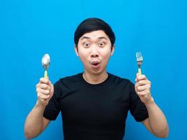 asiatico uomo Tenere posate sensazione eccitato di cena blu sfondo foto