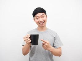 asiatico uomo sorridente e punto dito caffè tazza bianca sfondo foto