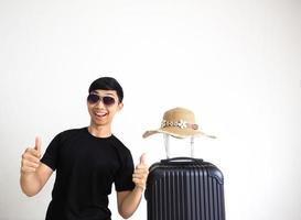 giovane asiatico uomo con occhiali da sole contento Sorridi e tonfi su con Vintage ▾ cappello sopra bagaglio nero colore su bianca isolato, turistico concetto foto