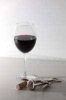 un bicchiere di vino e alcuni strumenti per il vino su una superficie di legno bianca. vino rosso foto