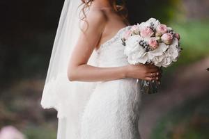 la sposa in un elegante abito da sposa tiene un bellissimo mazzo di fiori diversi e foglie verdi. tema del matrimonio foto