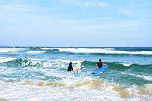 surfers coppia in attesa per il alto onde su spiaggia - sportivo persone con Surf tavole su il spiaggia - estremo sport e vacanza concetto foto