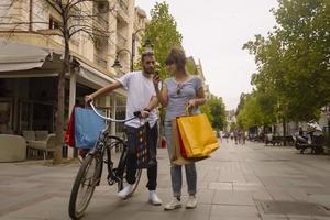 ritratto di allegro caucasico giovane coppia uomo e donna Tenere molti carta borse dopo shopping mentre a piedi e parlando su strada. contento famiglia coppia con pacchi all'aperto. acquisto concetto foto