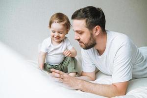 contento padre giovane uomo e bambino ragazza poco figlia avendo divertimento lettura un' libro nel bambini camera a casa foto