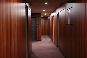 vuoto buio interno di il moderno Hotel corridoio, con rivestito in legno muri, elegante tappeti e illuminazione su il soffitto. foto