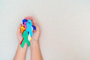 mondo cancro giorno, febbraio 4. mano Tenere blu, rosso, verde acqua, bianca, rosa, Marina Militare blu e giallo nastri per supporto persone vivente e malattia. assistenza sanitaria e autismo consapevolezza giorno concetto foto