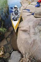 un' tre posti kayak con remi è parcheggiata su il roccioso riva di il lago con vita giacche qui vicino, su un' estate giorno. attivo riposo. foto