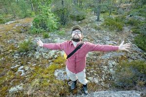 soddisfatto uomo con gioia diffusione il suo braccia per il lati, lui è su vacanza, a piedi nel il foresta godendo il fresco aria e natura. foto