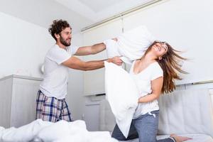 coppia avendo un' divertimento mentre cuscino combattere. giovane contento coppia battere il cuscini su il letto nel un' Camera da letto a casa. foto