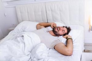 giovane uomo addormentato veglia su e allungamento nel il suo letto. le persone, di andare a dormire e riposo concetto - uomo dire bugie nel letto a casa, è tempo per scia su foto