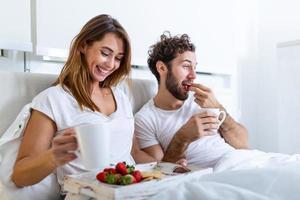 coppia nel amore avendo prima colazione nel letto. giovane caucasico coppia avendo romantico prima colazione nel letto. femmina e maschio , Due tazze di caffè, frutta e colorato biscotti. foto