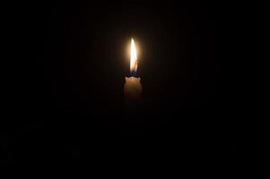 un' singolo ardente candela fiamma o leggero raggiante su un' bellissimo spirale bianca candela su nero o buio sfondo su tavolo nel Chiesa per Natale, funerale o memoriale servizio con copia spazio foto