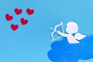san valentino giorno concetto. rosso cuori e Cupido mirando nel cuore su blu sfondo. creativo San Valentino giorno carta. foto