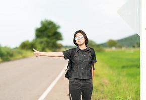 donna In piedi con zaino autostop lungo un' strada foto