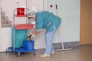 un adulto femmina addetto alle pulizie nel uniforme pulisce il corridoio di il Ospedale. foto