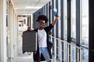 giovane africano americano femmina passanger nel casuale Abiti e cuffie è nel aeroporto con Bagaglio foto