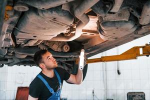 usi illuminazione attrezzatura. uomo nel opera uniforme riparazione bianca automobile al chiuso. concezione di automobile servizio foto