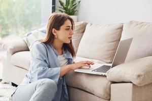 bellissimo giovane donna nel jeans e blu camicia dire bugie giù a divano con il computer portatile foto