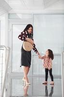 giovane madre con sua figlia a piedi insieme in casa nel il ufficio o aeroporto. avendo vacanza foto