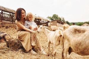 giovane madre con sua figlia è su il azienda agricola a estate con capre foto