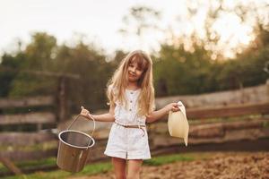 poco ragazza nel bianca Abiti è su il azienda agricola a estate all'aperto con latte foto