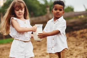 carino poco africano americano ragazzo con europeo ragazza è su il azienda agricola con latte foto