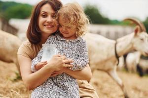 fresco naturale latte. giovane madre con sua figlia è su il azienda agricola a estate con capre foto