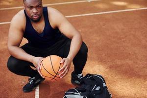 si siede con nero Borsa e preparazione per il gioco. africano americano uomo giochi pallacanestro su il Tribunale all'aperto foto