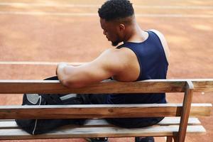 si siede con nero Borsa e preparazione per il gioco. africano americano uomo giochi pallacanestro su il Tribunale all'aperto foto