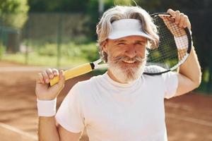 anziano moderno elegante uomo con racchetta all'aperto su tennis Tribunale a giorno foto