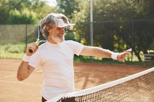 anziano moderno elegante uomo con racchetta all'aperto su tennis Tribunale a giorno foto