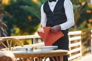 salviette piatti di rosso stoffa. nero Cameriere nel formale Abiti è a il suo opera all'aperto a soleggiato giorno foto