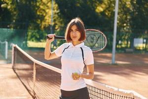 in piedi con racchetta nel mano. femmina tennis giocatore è su il Tribunale a giorno foto