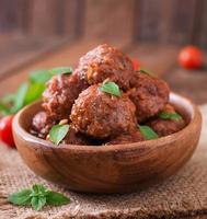 Polpette nel dolce e acida pomodoro salsa e basilico nel un' di legno ciotola foto