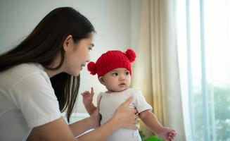 madre e neonato bambino indossare rosso cappelli nel il bianca Camera da letto, caldo luce del sole nel il sera di il giorno foto