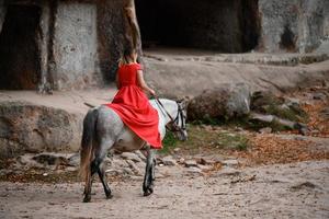 colomba rocce e cavallo cavalcare, un' donna equitazione un' cavallo nel un' rosso vestito con spoglio piedi. foto