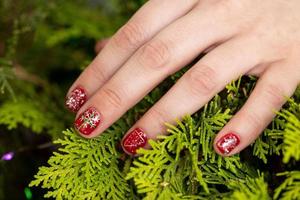 un' avvicinamento di rosso chiodo manicure design con fiocco di neve su Natale albero foto