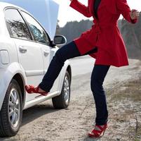 arrabbiato donna calci auto ruota dopo auto incidente o alcuni rotto scorta parte foto