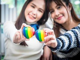 selettivo messa a fuoco, giovane asiatico lesbica coppia Tenere un' arcobaleno cuore simboleggia il lgbt Comunità, nel il vivente camera a casa, il stile di vita di coppia lgbt amorevole donne contento nel romantico amore e divertimento foto