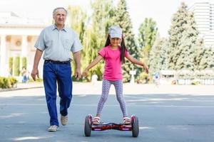 poco sorridente ragazza apprendimento per cavalcata un' hoverboard con sua genitori all'aperto foto