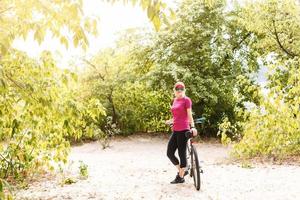 bicicletta adolescente con le signore Bici nel estate parco. Da donna strada bicicletta per in esecuzione su natura. adolescente ragazza nel casco Ciclismo guado attraverso acqua. ragazza trasporta pesi su bicicletta foto