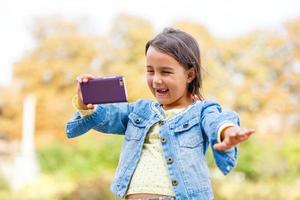 video streaming. adorabile bambino apprendimento nuovo tecnologia. poco ragazza utilizzando mobile Telefono. piccolo ragazza bambino con smartphone. carino mobile Telefono tecnologia utente. Guardando video su mobile dispositivo. foto