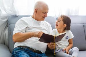 contento poco ragazza con nonno lettura storia libro a casa foto