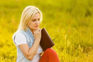 un' caucasico giovane cristiano donna lettura un' Bibbia all'aperto nel un' pubblico parco. foto