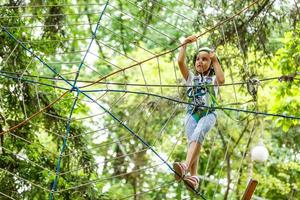 adorabile poco ragazza godendo sua tempo nel arrampicata avventura parco su caldo e soleggiato estate giorno foto